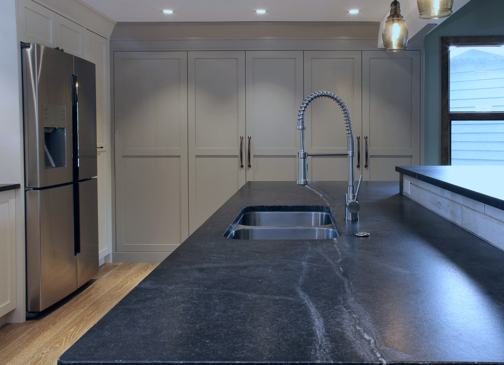 Example of a large transitional u-shaped medium tone wood floor open concept kitchen design in Calgary with an undermount sink, shaker cabinets, soapstone countertops, ceramic backsplash, stainless steel appliances and an island
