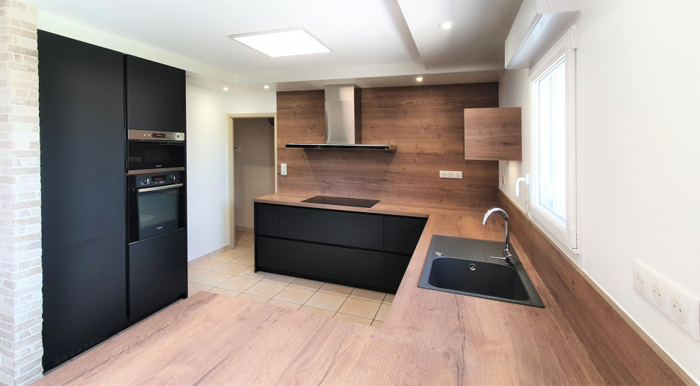 This is an example of a large modern galley open plan kitchen in Other with terra-cotta floors, beige floor, recessed, an undermount sink, flat-panel cabinets, black cabinets, laminate benchtops, brown splashback, timber splashback, panelled appliances, with island and brown benchtop.