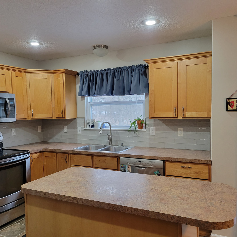 Example of a mid-sized l-shaped vinyl floor and multicolored floor eat-in kitchen design with a double-bowl sink, flat-panel cabinets, light wood cabinets, laminate countertops, gray backsplash, ceramic backsplash, stainless steel appliances, an island and multicolored countertops
