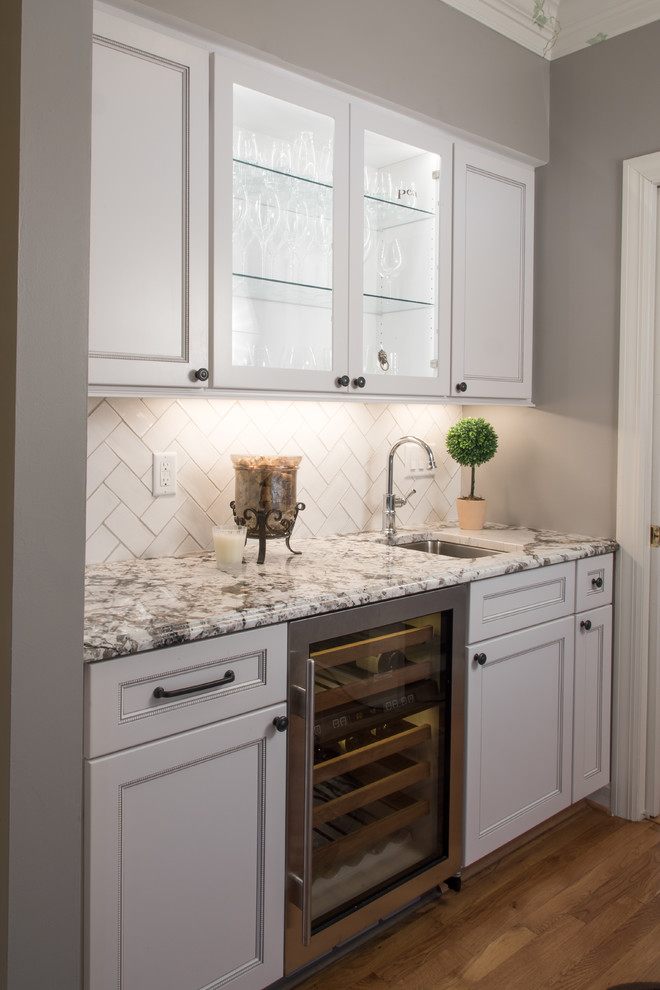 This is an example of a transitional single-wall wet bar in St Louis with an undermount sink, flat-panel cabinets, white cabinets, granite benchtops, white splashback, subway tile splashback and medium hardwood floors.