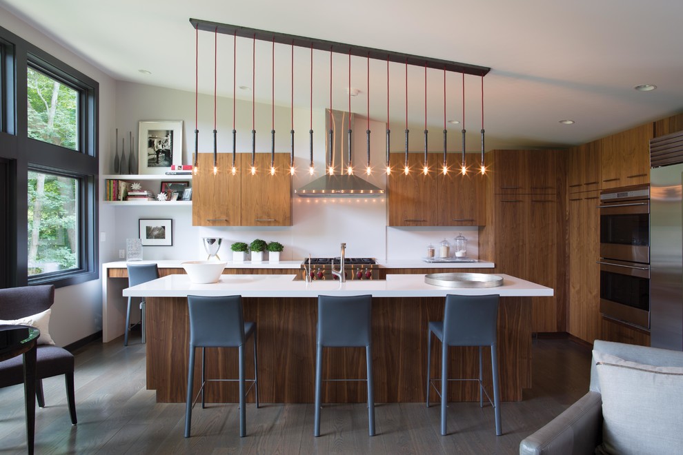 Mid-sized contemporary l-shaped eat-in kitchen in New York with flat-panel cabinets, medium wood cabinets, stainless steel appliances, with island, white splashback, a farmhouse sink, solid surface benchtops, dark hardwood floors, brown floor and white benchtop.