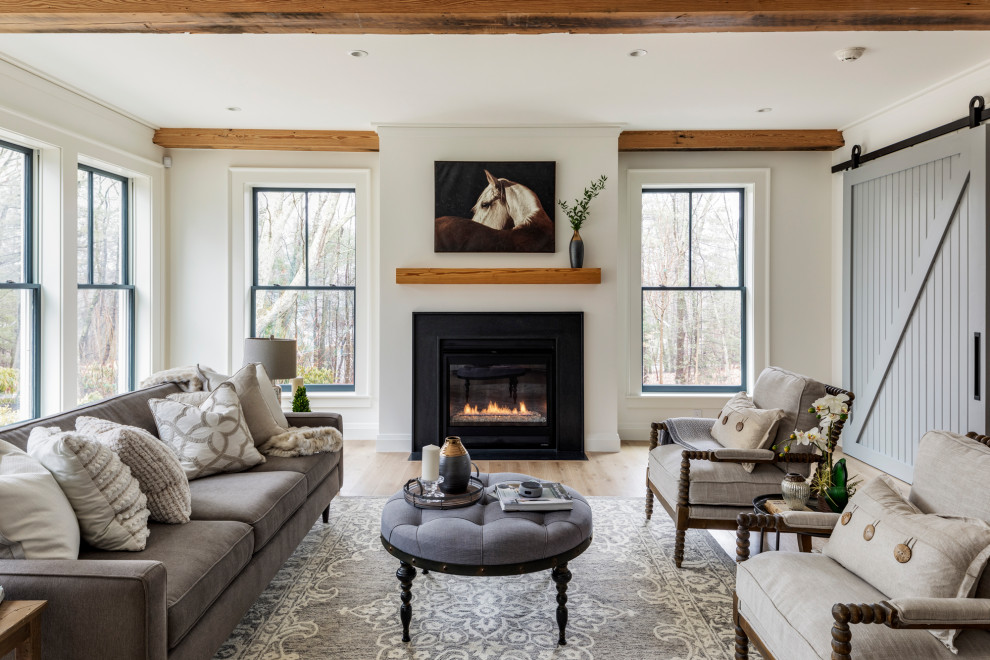 Photo of a large country formal living room in Boston with white walls, light hardwood floors, a standard fireplace, a metal fireplace surround, no tv and exposed beam.