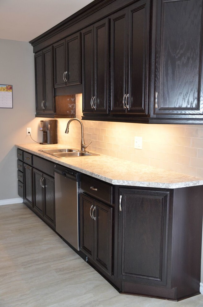 Small transitional galley vinyl floor and gray floor enclosed kitchen photo with a drop-in sink, recessed-panel cabinets, dark wood cabinets, laminate countertops, glass tile backsplash, stainless steel appliances and no island