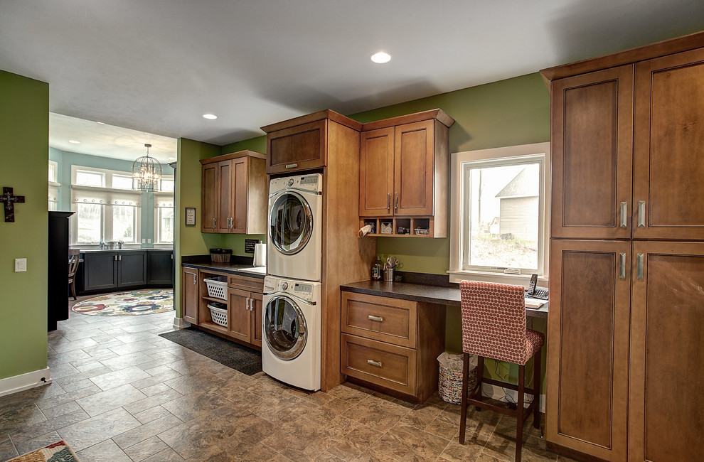 Inspiration for a large arts and crafts single-wall utility room in Grand Rapids with a drop-in sink, medium wood cabinets, solid surface benchtops, green walls, ceramic floors and a stacked washer and dryer.