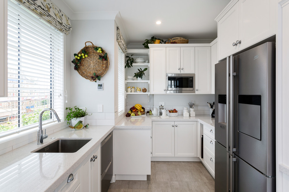 This is an example of a large traditional galley eat-in kitchen in Auckland with an undermount sink, recessed-panel cabinets, white cabinets, quartz benchtops, white splashback, porcelain splashback, stainless steel appliances, medium hardwood floors, with island and brown floor.