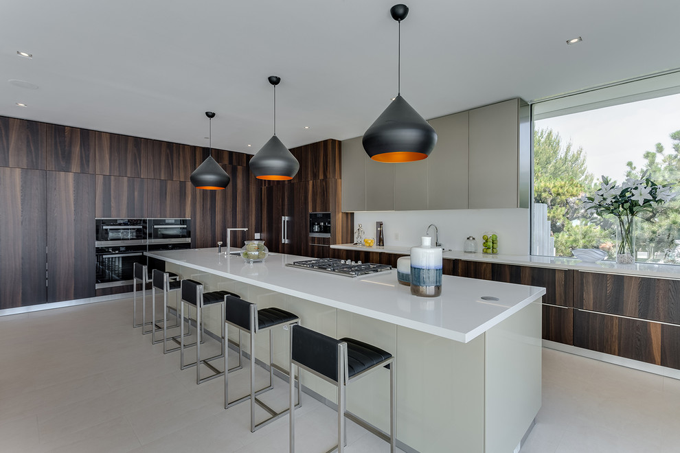 Large contemporary kitchen in Los Angeles with flat-panel cabinets, dark wood cabinets, quartz benchtops, white splashback, black appliances, ceramic floors, with island, beige floor and an undermount sink.