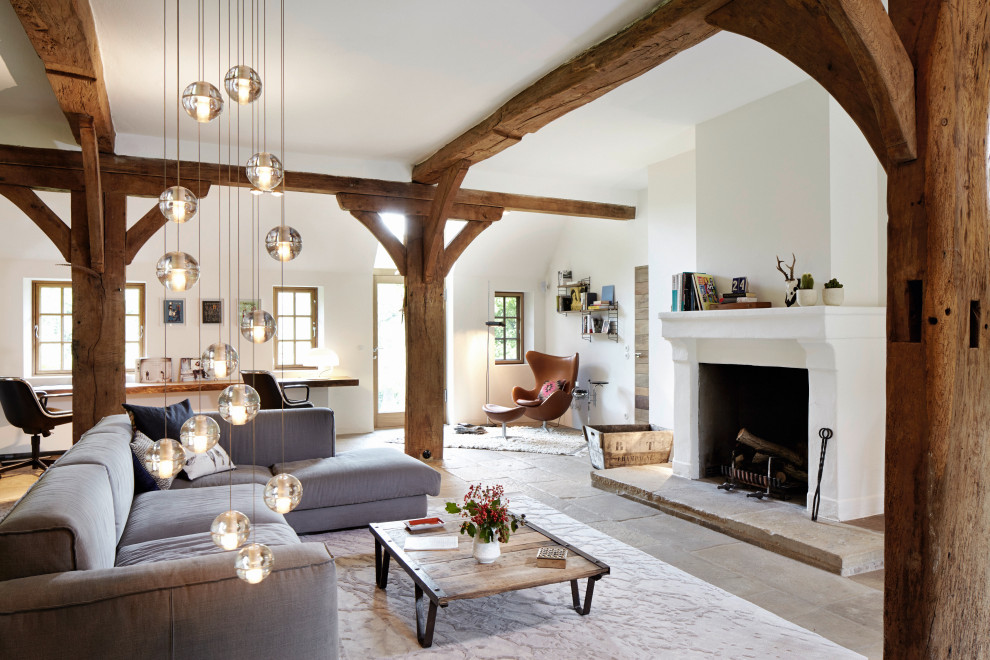 This is an example of a country open concept living room in Hamburg with white walls, a standard fireplace, grey floor and exposed beam.