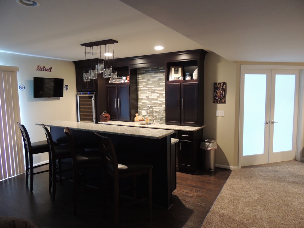 This is an example of a mid-sized traditional single-wall seated home bar in Detroit with shaker cabinets, dark wood cabinets, granite benchtops, glass tile splashback, dark hardwood floors and beige splashback.