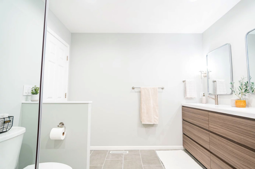 This is an example of a medium sized traditional ensuite bathroom in Minneapolis with flat-panel cabinets, medium wood cabinets, a corner bath, a corner shower, a one-piece toilet, grey tiles, grey walls, ceramic flooring, a submerged sink, engineered stone worktops, grey floors, a sliding door, white worktops, double sinks and a freestanding vanity unit.