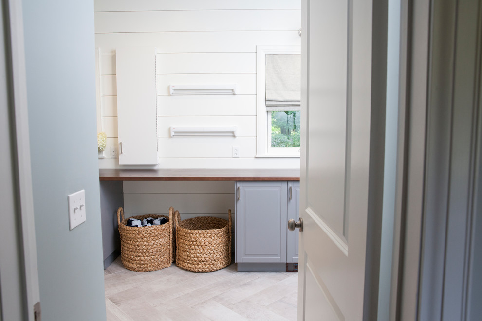 Design ideas for a large traditional u-shaped dedicated laundry room in New York with raised-panel cabinets, grey cabinets, wood benchtops, porcelain floors, a side-by-side washer and dryer, grey floor and white walls.