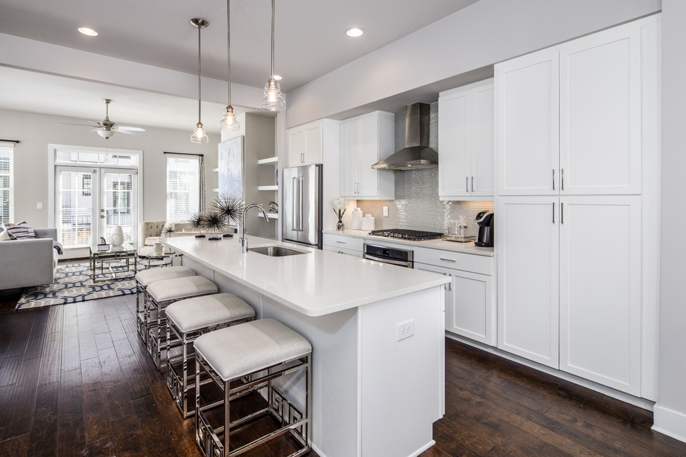 Design ideas for a contemporary galley kitchen in Atlanta with an undermount sink, shaker cabinets, white cabinets, grey splashback, glass tile splashback, stainless steel appliances, dark hardwood floors, with island, brown floor and white benchtop.