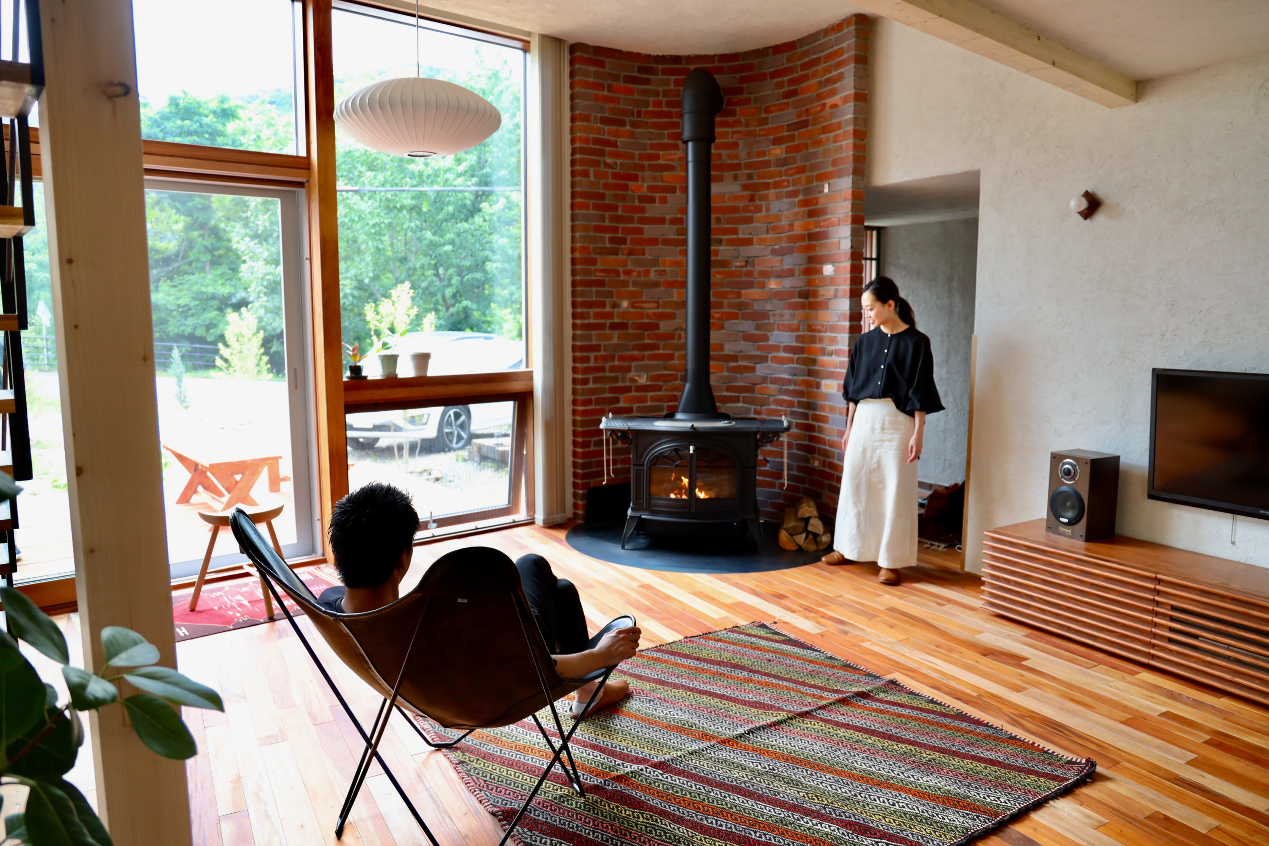 Mid-sized open concept medium tone wood floor, brown floor and tray ceiling living room photo in Sapporo with beige walls, a wood stove, a brick fireplace and a wall-mounted tv