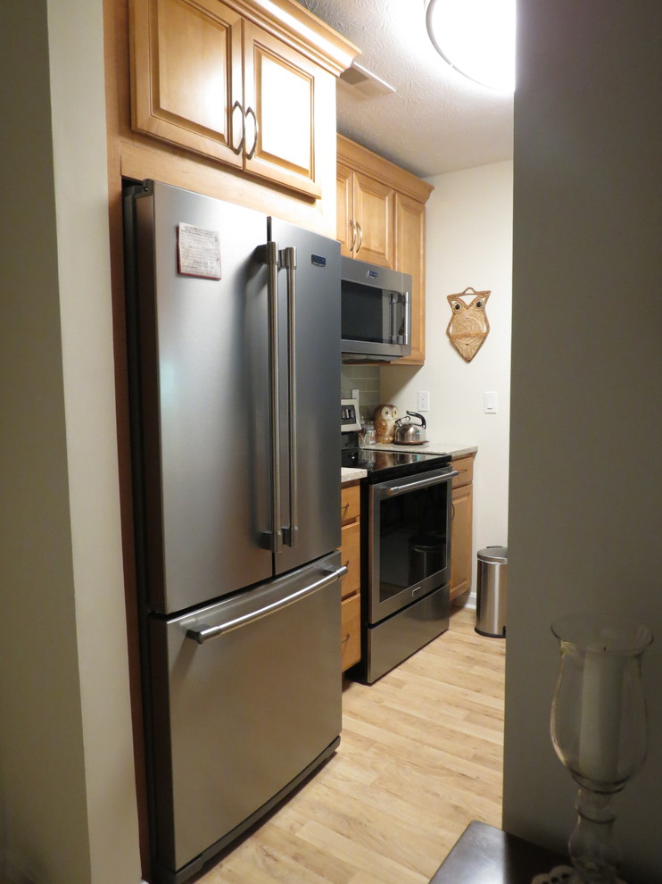 Enclosed kitchen - small transitional galley vinyl floor and brown floor enclosed kitchen idea with an undermount sink, raised-panel cabinets, light wood cabinets, quartz countertops, beige backsplash, glass tile backsplash, stainless steel appliances, no island and beige countertops