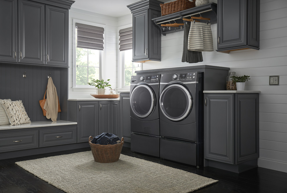 Photo of a mid-sized traditional l-shaped dedicated laundry room in Cincinnati with raised-panel cabinets, grey cabinets, white walls, dark hardwood floors, a side-by-side washer and dryer, black floor and white benchtop.