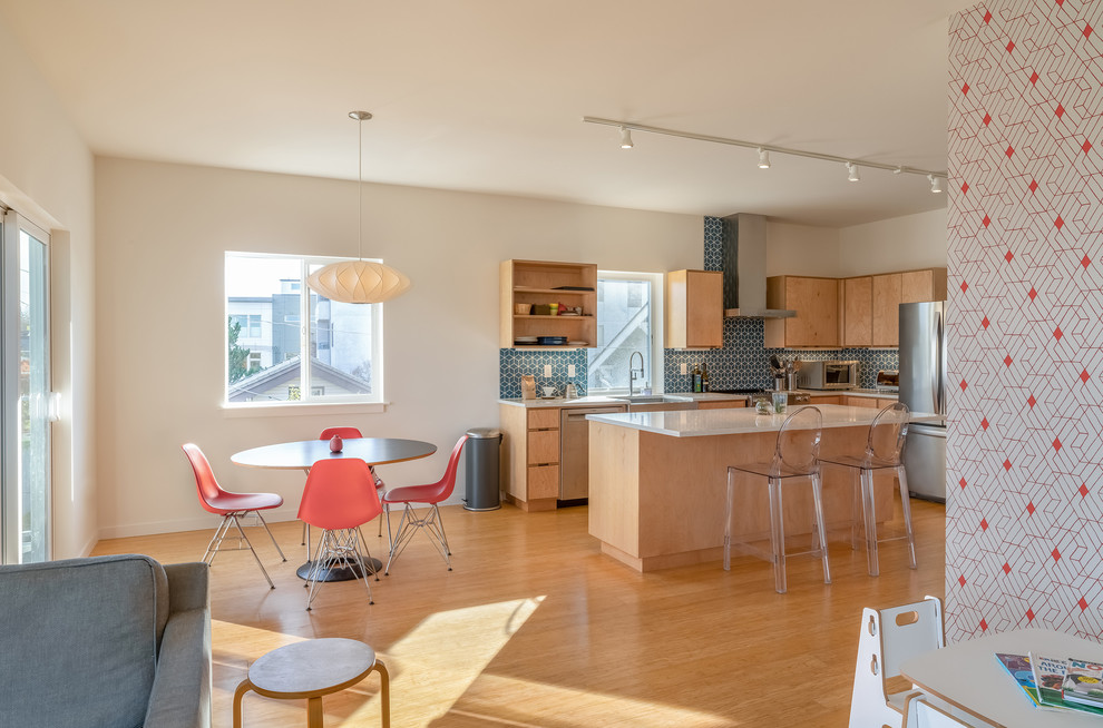 This is an example of a mid-sized modern l-shaped open plan kitchen in Seattle with a farmhouse sink, flat-panel cabinets, light wood cabinets, quartz benchtops, blue splashback, cement tile splashback, stainless steel appliances, bamboo floors, with island, brown floor and white benchtop.