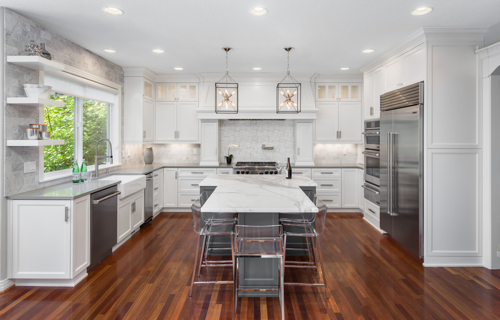 Inspiration for a transitional u-shaped kitchen in Portland with a farmhouse sink, shaker cabinets, white cabinets, white splashback, stainless steel appliances, dark hardwood floors and with island.