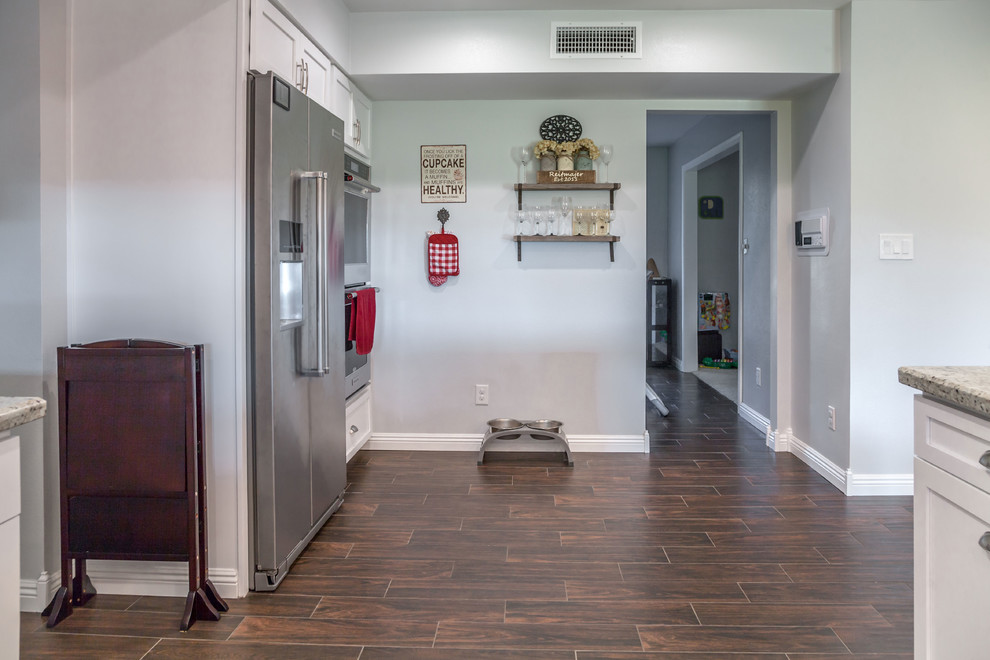 Example of a mid-sized transitional u-shaped laminate floor and brown floor open concept kitchen design in Phoenix with an undermount sink, recessed-panel cabinets, white cabinets, granite countertops, multicolored backsplash, mosaic tile backsplash and stainless steel appliances