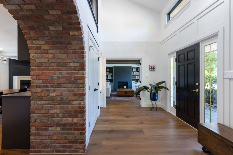 Mid-sized transitional medium tone wood floor, brown floor and wall paneling foyer photo in Vancouver with white walls and a black front door