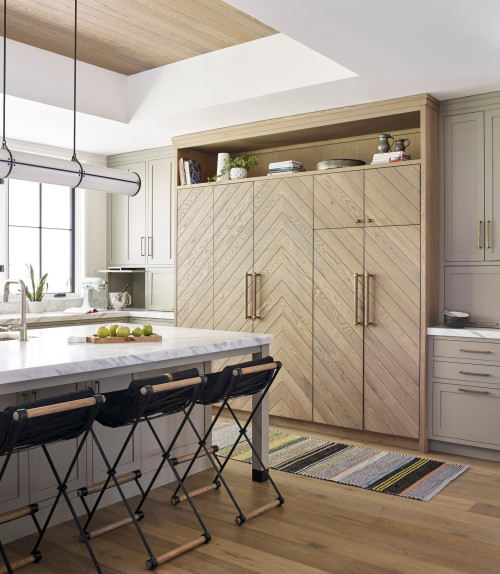 Contemporary kitchen with chevron wood kitchen cabinet wall, marble island, and black bar stools on light wood flooring.