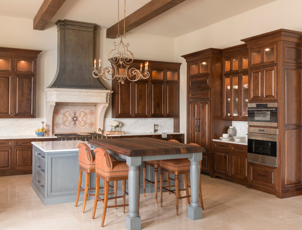 This is an example of a large mediterranean l-shaped eat-in kitchen in Atlanta with a farmhouse sink, raised-panel cabinets, medium wood cabinets, white splashback, stone slab splashback, panelled appliances, with island, limestone floors and marble benchtops.