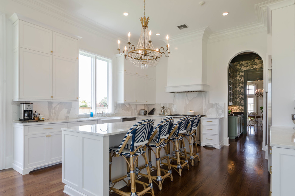 Design ideas for a mid-sized beach style u-shaped kitchen in New Orleans with a farmhouse sink, raised-panel cabinets, white cabinets, marble benchtops, white splashback, stainless steel appliances, dark hardwood floors and with island.