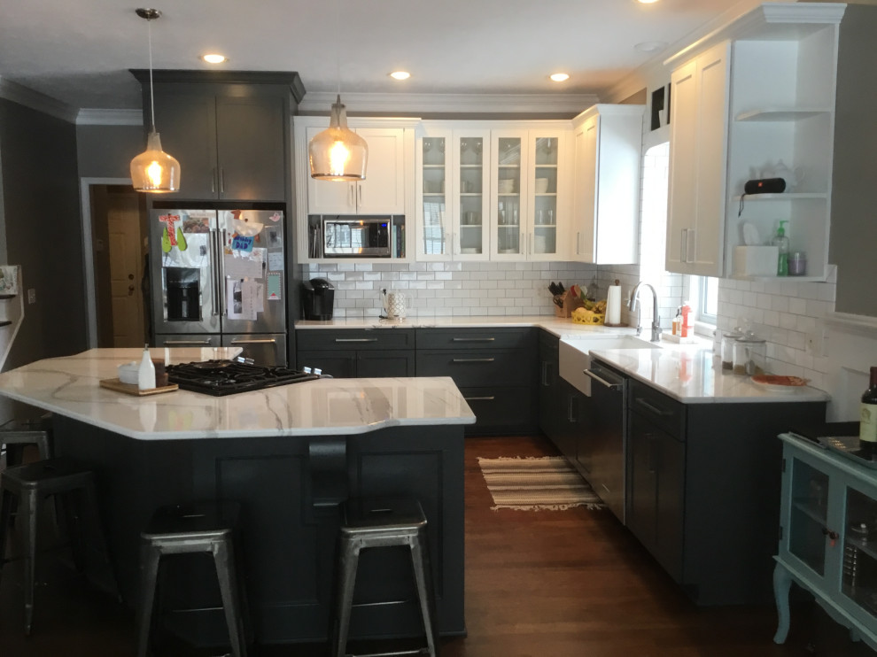 This is an example of a mid-sized transitional l-shaped eat-in kitchen in Other with a farmhouse sink, recessed-panel cabinets, grey cabinets, white splashback, stainless steel appliances, with island, white benchtop, quartz benchtops, subway tile splashback, dark hardwood floors and red floor.
