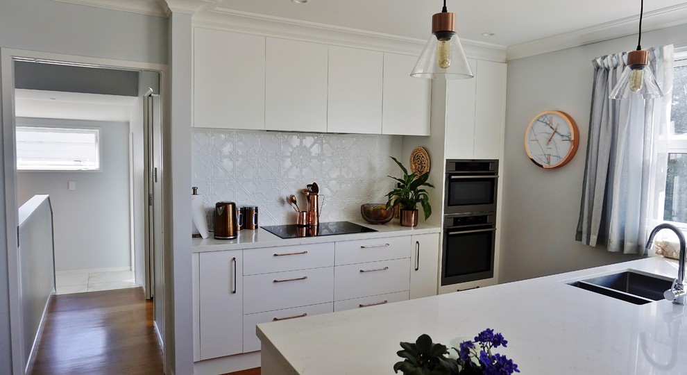 Photo of a large single-wall eat-in kitchen in Auckland with a triple-bowl sink, raised-panel cabinets, white cabinets, granite benchtops, white splashback, metal splashback, stainless steel appliances, medium hardwood floors, with island, brown floor and white benchtop.