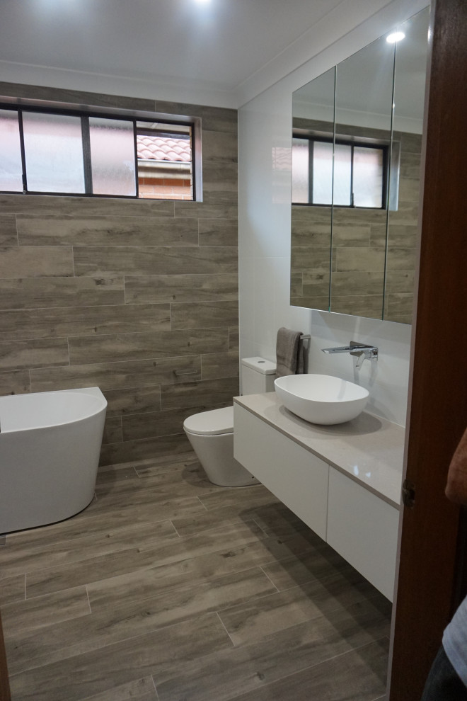 This is an example of a mid-sized modern master bathroom in Sydney with white cabinets, a freestanding tub, an open shower, a two-piece toilet, white tile, ceramic tile, white walls, ceramic floors, a drop-in sink, engineered quartz benchtops, grey floor, an open shower, grey benchtops, a single vanity and a floating vanity.