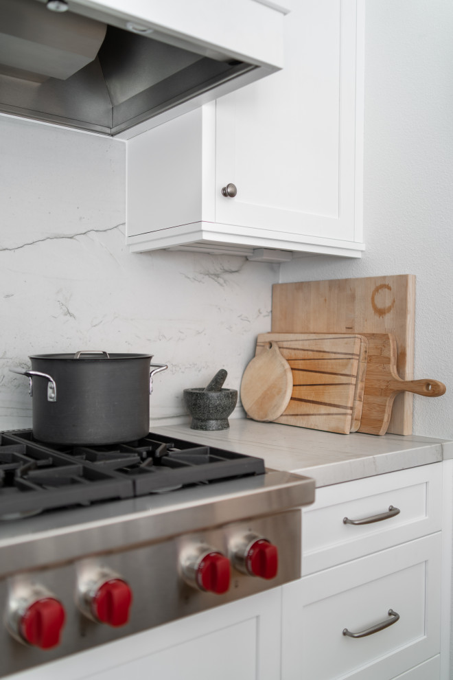 Example of a mid-sized classic galley medium tone wood floor and brown floor open concept kitchen design in Denver with a farmhouse sink, recessed-panel cabinets, white cabinets, quartzite countertops, white backsplash, stone slab backsplash, stainless steel appliances, an island and white countertops