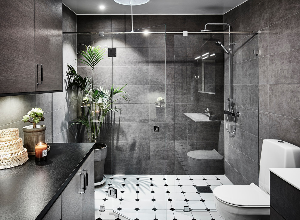 Photo of a mid-sized contemporary 3/4 bathroom in Gothenburg with flat-panel cabinets, medium wood cabinets, a one-piece toilet, gray tile, ceramic tile, ceramic floors, a trough sink, laminate benchtops, an alcove shower, grey walls, white floor and a hinged shower door.