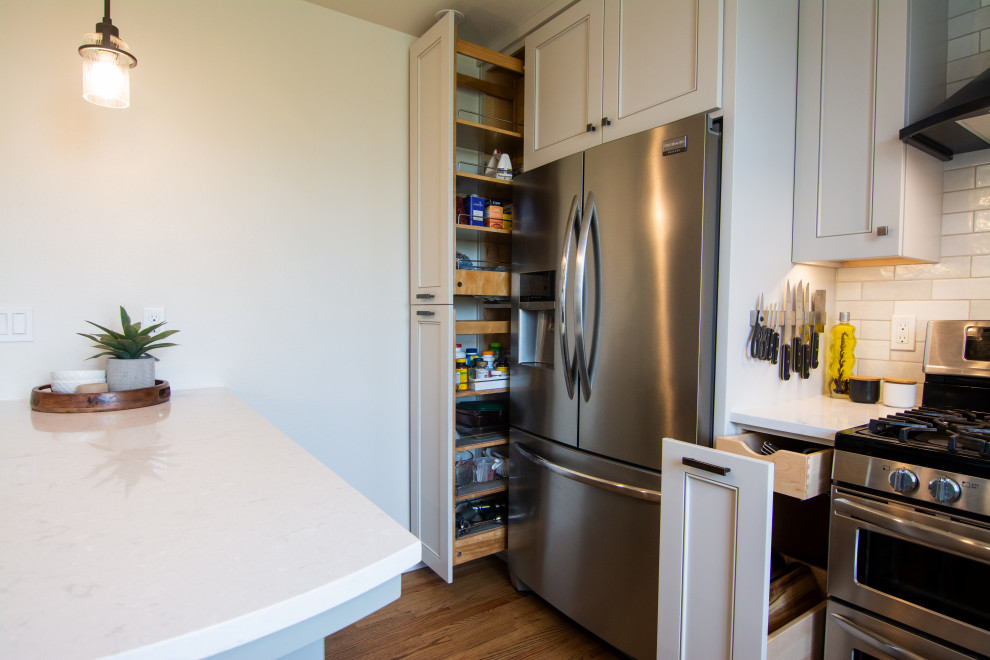 Mid-sized transitional l-shaped medium tone wood floor and brown floor kitchen photo with an undermount sink, recessed-panel cabinets, gray cabinets, quartz countertops, white backsplash, ceramic backsplash, stainless steel appliances, a peninsula and white countertops