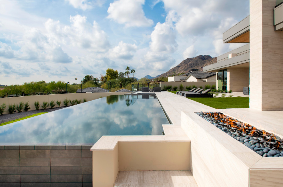 Diseño de piscina infinita contemporánea extra grande rectangular en patio trasero con paisajismo de piscina y adoquines de piedra natural