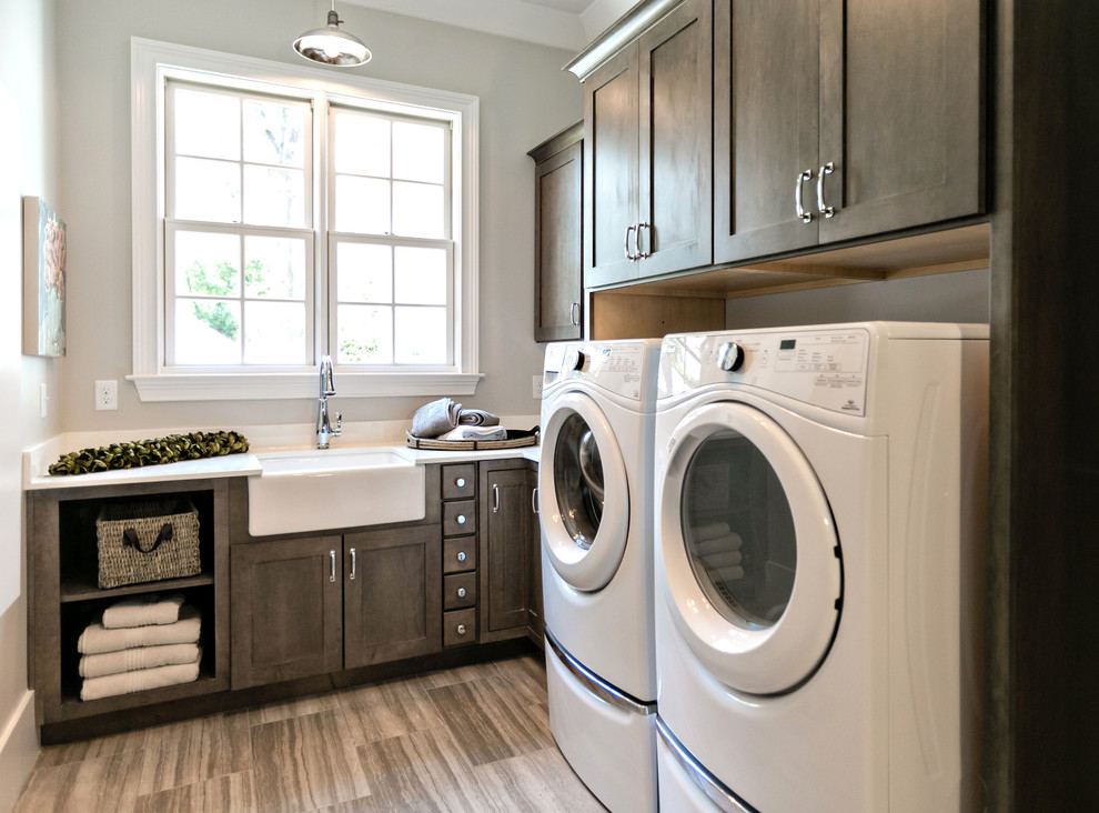 Photo of a small transitional l-shaped dedicated laundry room in St Louis with a farmhouse sink, shaker cabinets, dark wood cabinets, grey walls, a side-by-side washer and dryer, beige floor, porcelain floors, quartz benchtops and white benchtop.