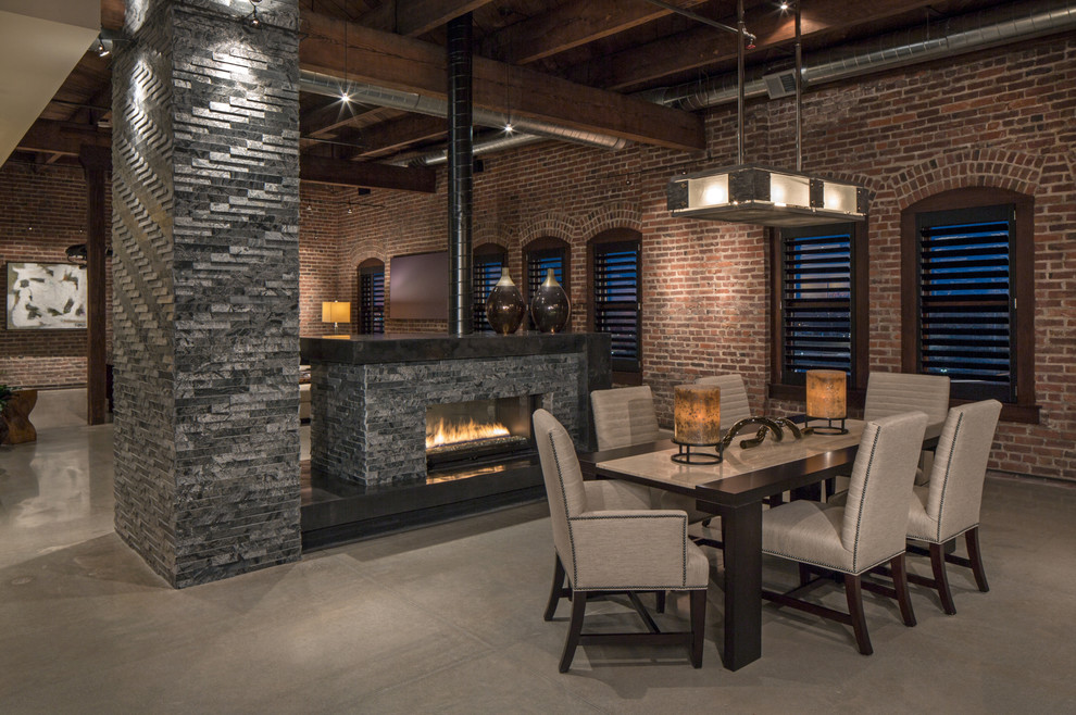 Inspiration for an industrial dining room in Omaha with concrete floors and a two-sided fireplace.