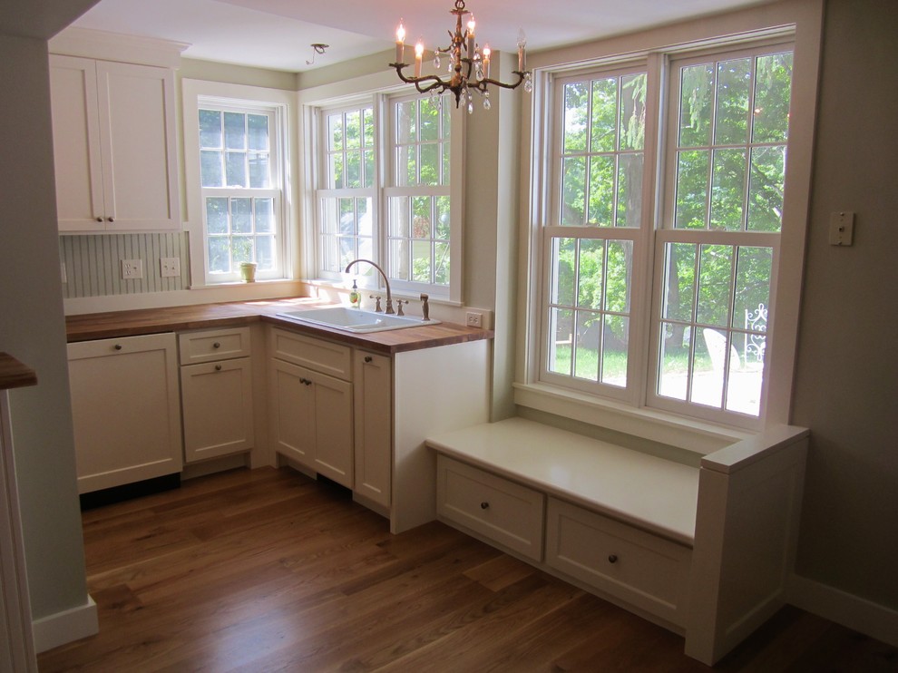 Country kitchen in New York with shaker cabinets, with island, a drop-in sink, white cabinets, wood benchtops, white appliances and medium hardwood floors.