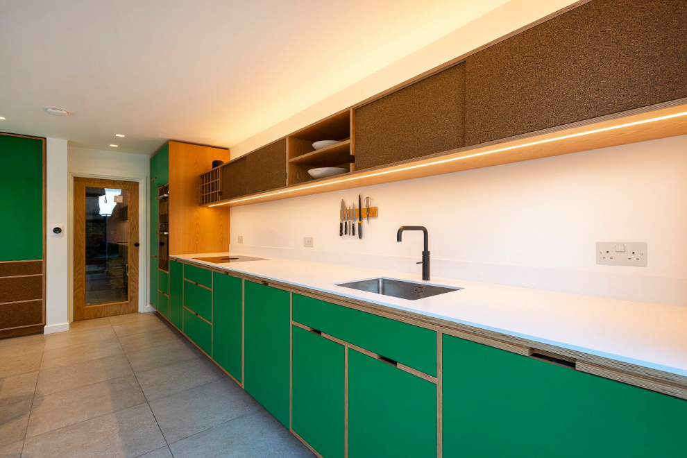 Example of a mid-sized danish single-wall porcelain tile and gray floor eat-in kitchen design in London with an integrated sink, recessed-panel cabinets, green cabinets, paneled appliances, no island and white countertops