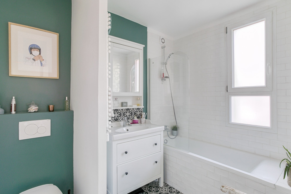 Example of a mid-sized trendy master white tile and terra-cotta tile wallpaper, cement tile floor, black floor and single-sink tub/shower combo design in Paris with beaded inset cabinets, white cabinets, an undermount tub, a wall-mount toilet, green walls, an undermount sink, a hinged shower door, white countertops and a freestanding vanity