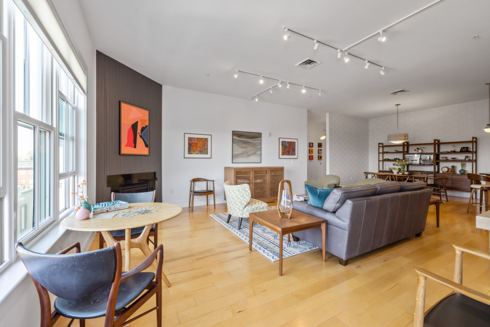 Mid-sized midcentury open concept living room in Portland Maine with white walls, light hardwood floors, a corner fireplace, a wood fireplace surround, a concealed tv and wood walls.