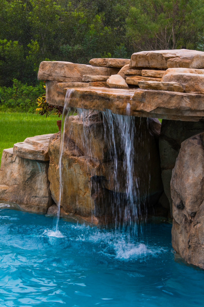 This is an example of a large tropical backyard custom-shaped natural pool in Tampa with a water feature and natural stone pavers.