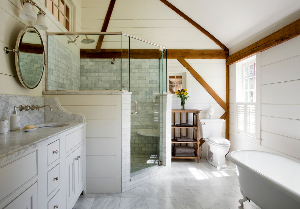 This is an example of a mid-sized country master bathroom in Boston with white cabinets, marble benchtops, a claw-foot tub, a corner shower, white tile, ceramic tile, white walls, marble floors, an undermount sink, beaded inset cabinets and a two-piece toilet.