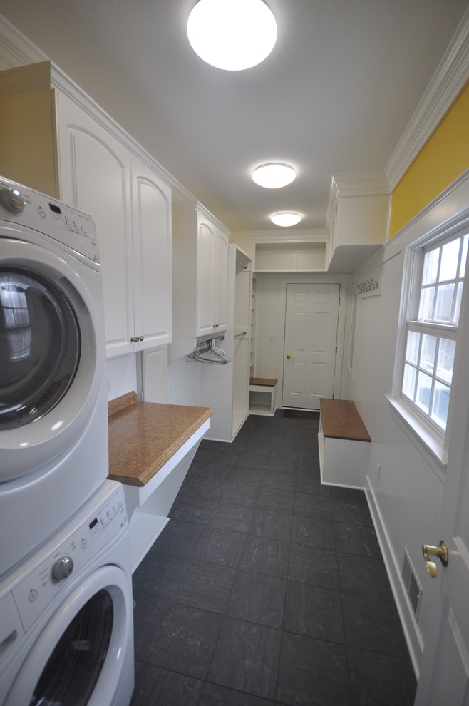Small traditional galley utility room in Other with raised-panel cabinets, white cabinets, laminate benchtops, yellow walls, ceramic floors and a stacked washer and dryer.