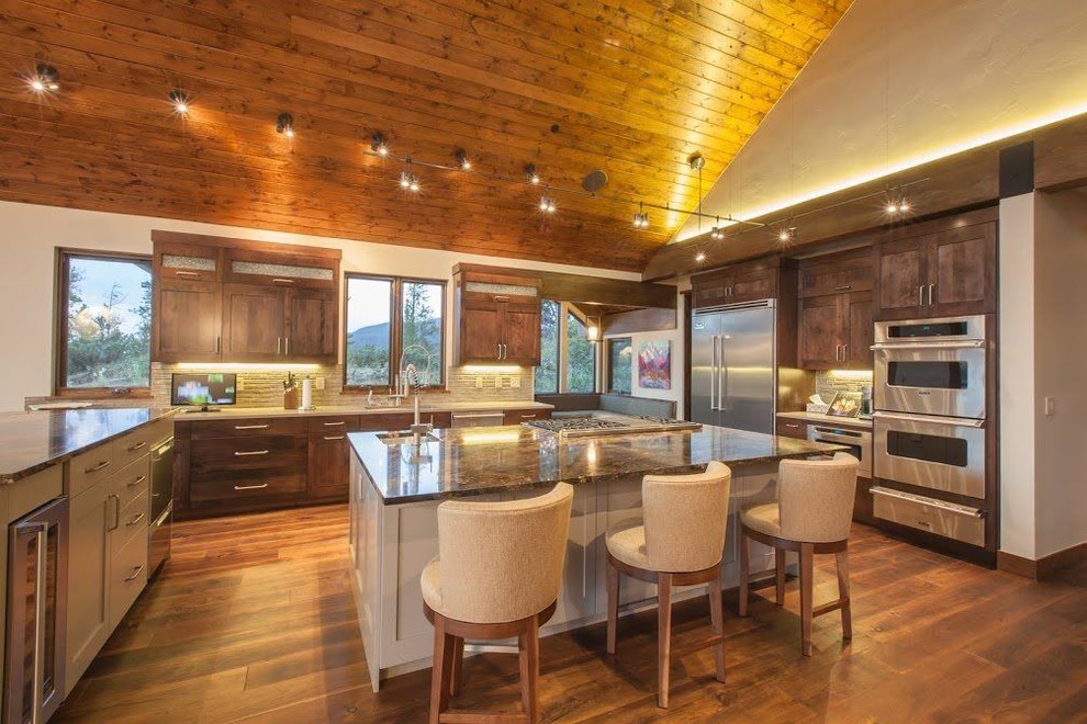 Open concept kitchen - large rustic u-shaped medium tone wood floor and brown floor open concept kitchen idea in Denver with an undermount sink, shaker cabinets, medium tone wood cabinets, granite countertops, beige backsplash, stone tile backsplash, stainless steel appliances and an island