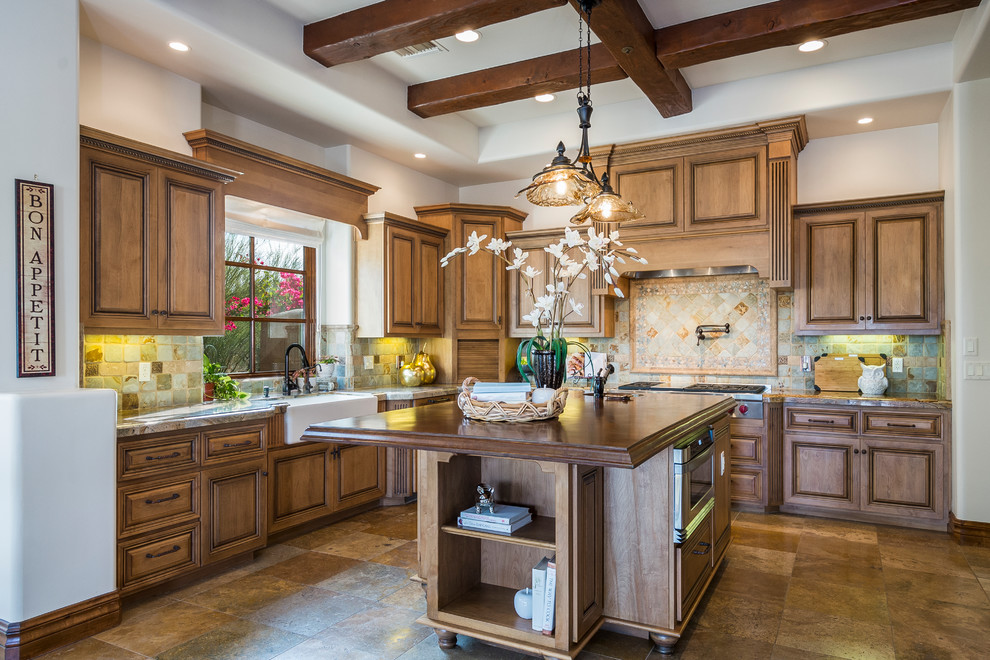 This is an example of a mediterranean l-shaped kitchen in Phoenix with a farmhouse sink, raised-panel cabinets, dark wood cabinets, with island and brown floor.