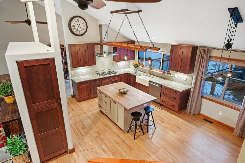 Inspiration for a mid-sized transitional u-shaped medium tone wood floor and multicolored floor kitchen remodel in Denver with a farmhouse sink, shaker cabinets, brown cabinets, granite countertops, beige backsplash, subway tile backsplash, stainless steel appliances, an island and multicolored countertops
