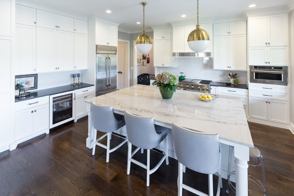 Inspiration for a large transitional u-shaped dark wood floor and brown floor kitchen remodel in Chicago with an undermount sink, white backsplash, ceramic backsplash, stainless steel appliances, black countertops, shaker cabinets, white cabinets, solid surface countertops and an island