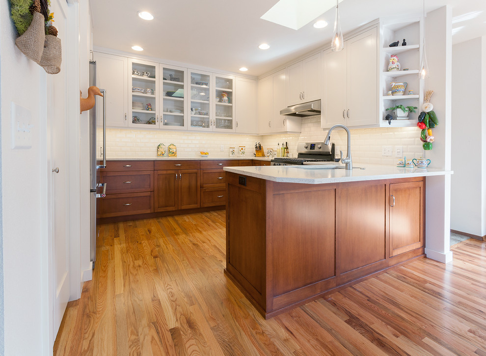 Example of a transitional light wood floor kitchen design with a double-bowl sink, shaker cabinets, quartz countertops, white backsplash, subway tile backsplash and stainless steel appliances