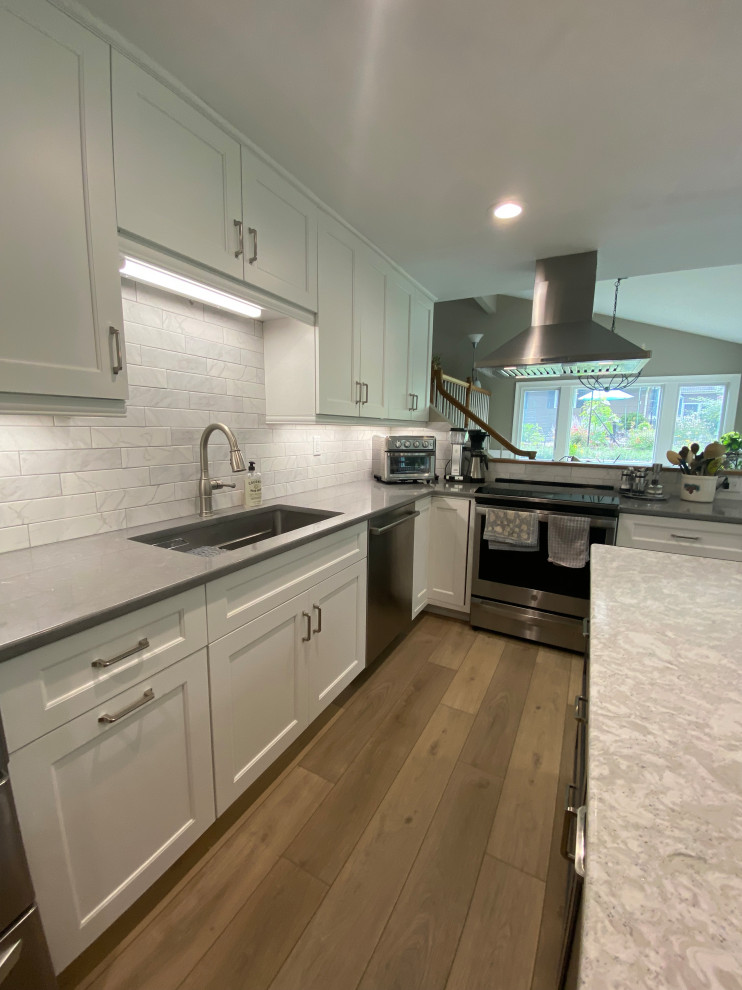 Mid-sized l-shaped eat-in kitchen in New York with an undermount sink, shaker cabinets, white cabinets, quartz benchtops, white splashback, porcelain splashback, stainless steel appliances, laminate floors, with island, yellow floor and grey benchtop.