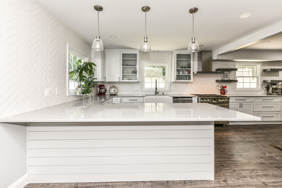 This is an example of a large modern galley eat-in kitchen in DC Metro with a farmhouse sink, shaker cabinets, white cabinets, quartzite benchtops, white splashback, porcelain splashback, stainless steel appliances, vinyl floors, with island, brown floor and grey benchtop.