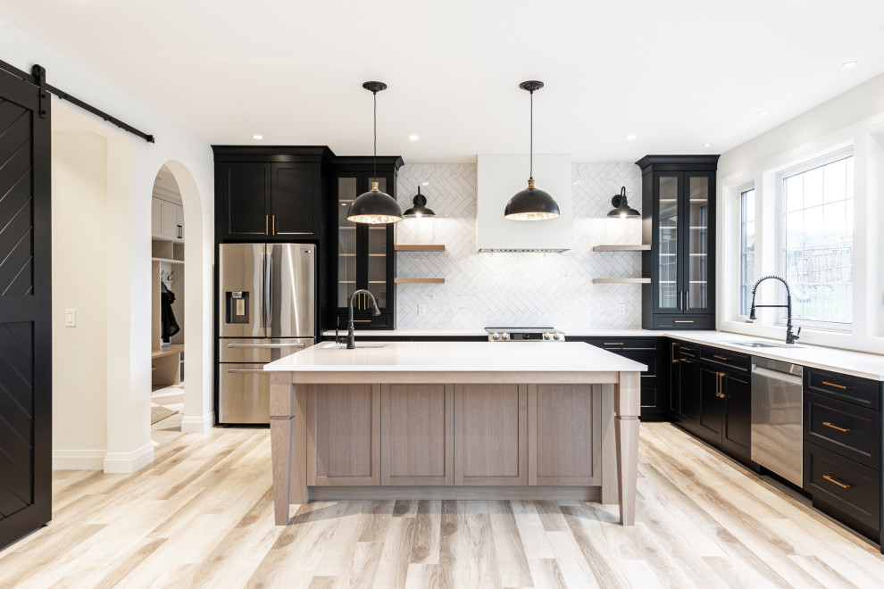 Inspiration for a mid-sized transitional l-shaped laminate floor and brown floor eat-in kitchen remodel in Toronto with an undermount sink, recessed-panel cabinets, black cabinets, quartz countertops, white backsplash, ceramic backsplash, stainless steel appliances, an island and white countertops