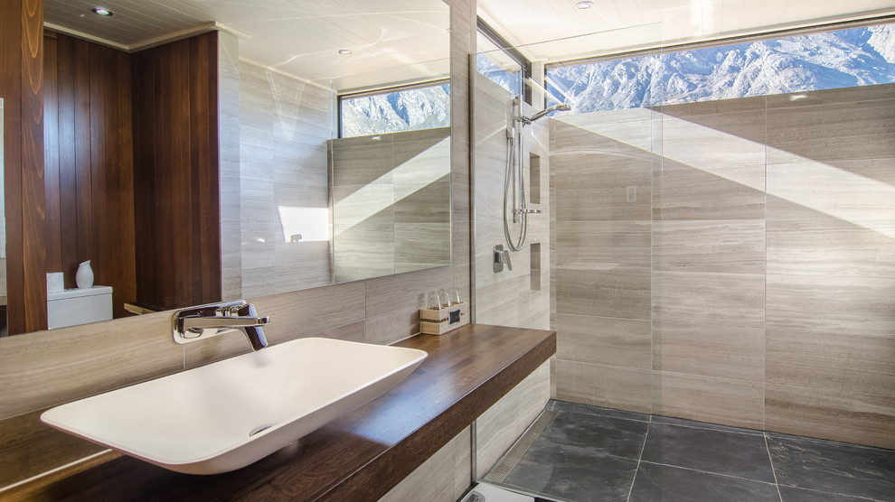 Photo of a contemporary bathroom in Auckland with an open shower, beige tile, beige walls, a vessel sink, wood benchtops and an open shower.